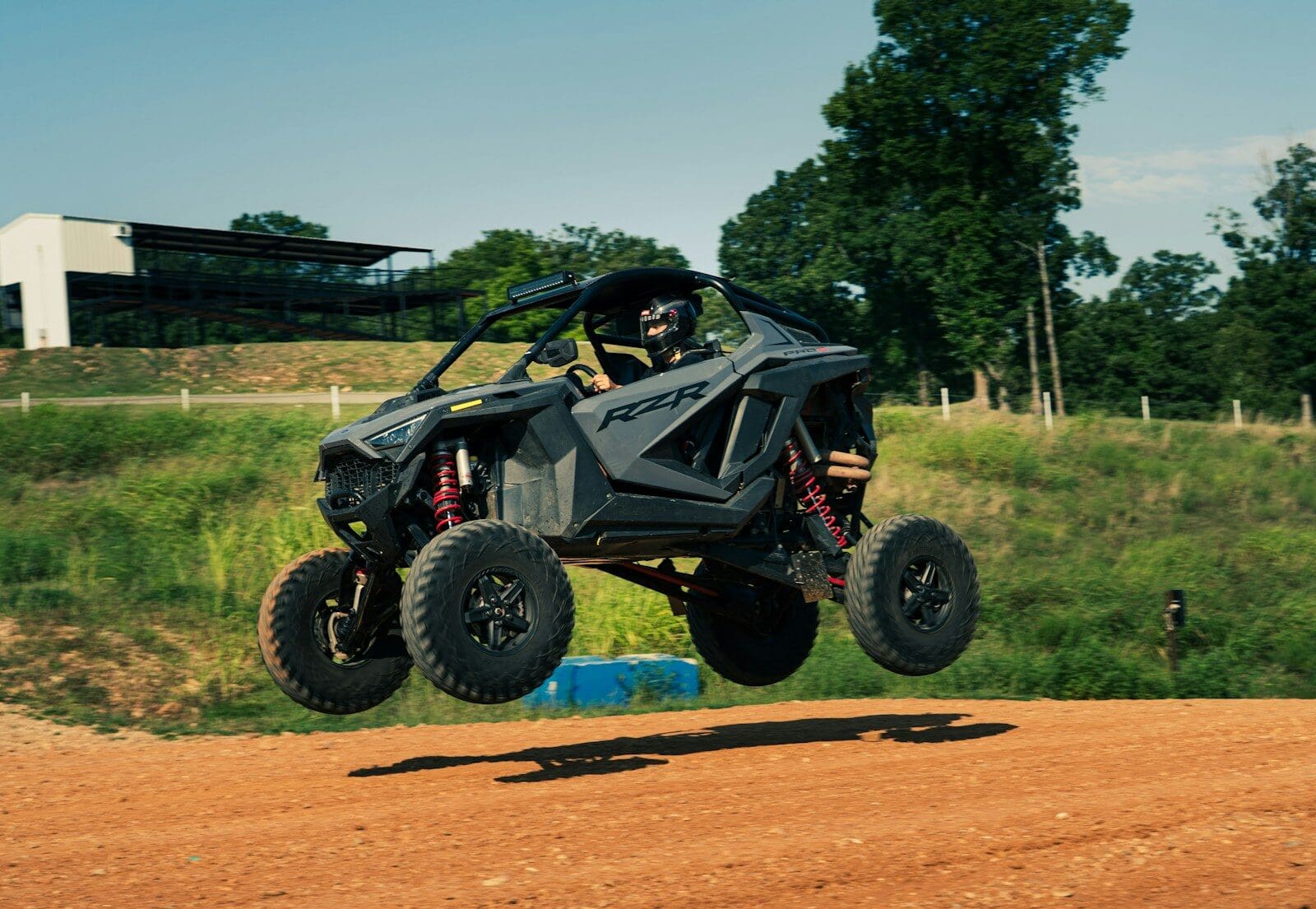 A dark gray rzr vehicle jumps over a dirt track
